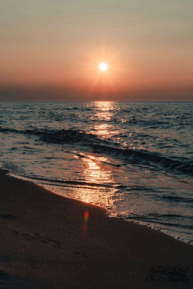 Low angle view of sunset over a lake with a lens flare on the sand. 