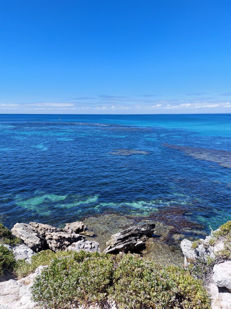 A very blue sky and blue water with coral and rock outcrops.