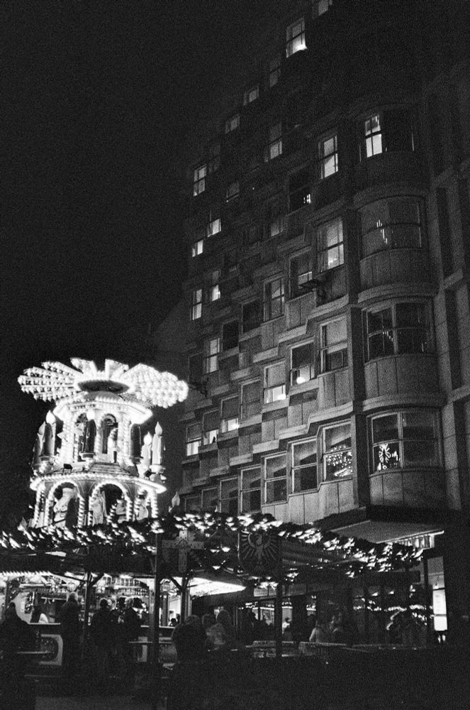 A mid-century concrete and glass building lit up in the dark by a Xmas structure covered in lots of small, white lights.
