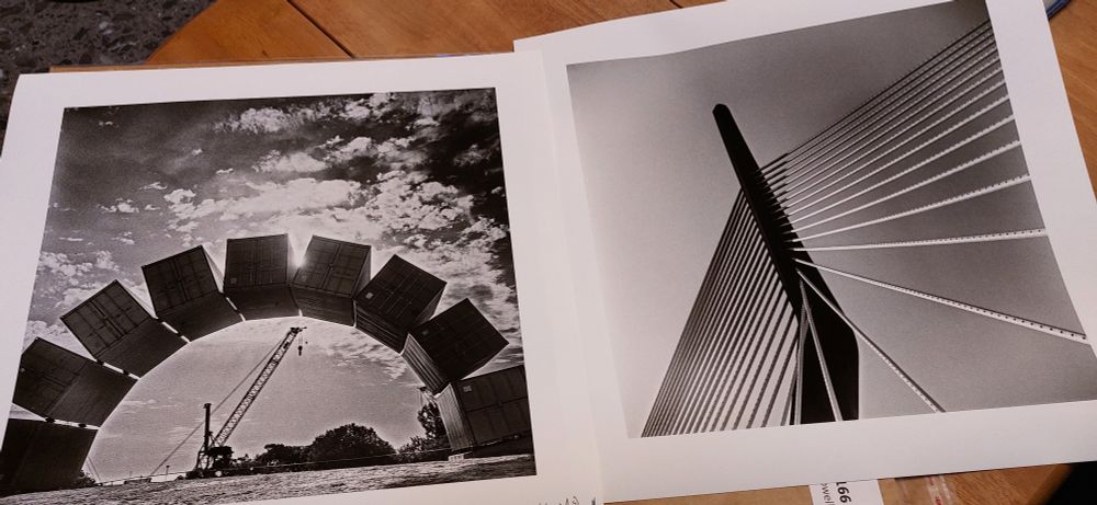 2 square format black and white images next to each other, unframed, lying on a table. 