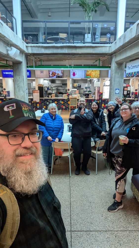 A group of urban sketchers in a food court of the Westside Bazaar in Buffalo, NY with food booths behind them.