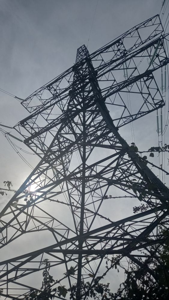 An electricity high-tension transmission tower ("pylon") silhouetted against a grey sky.