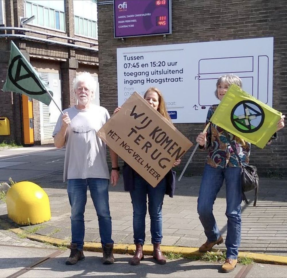 Rebellen voor de fabriek van Ofi, met XR vlaggen en met een bord "wij komen terug met nog veel meer".