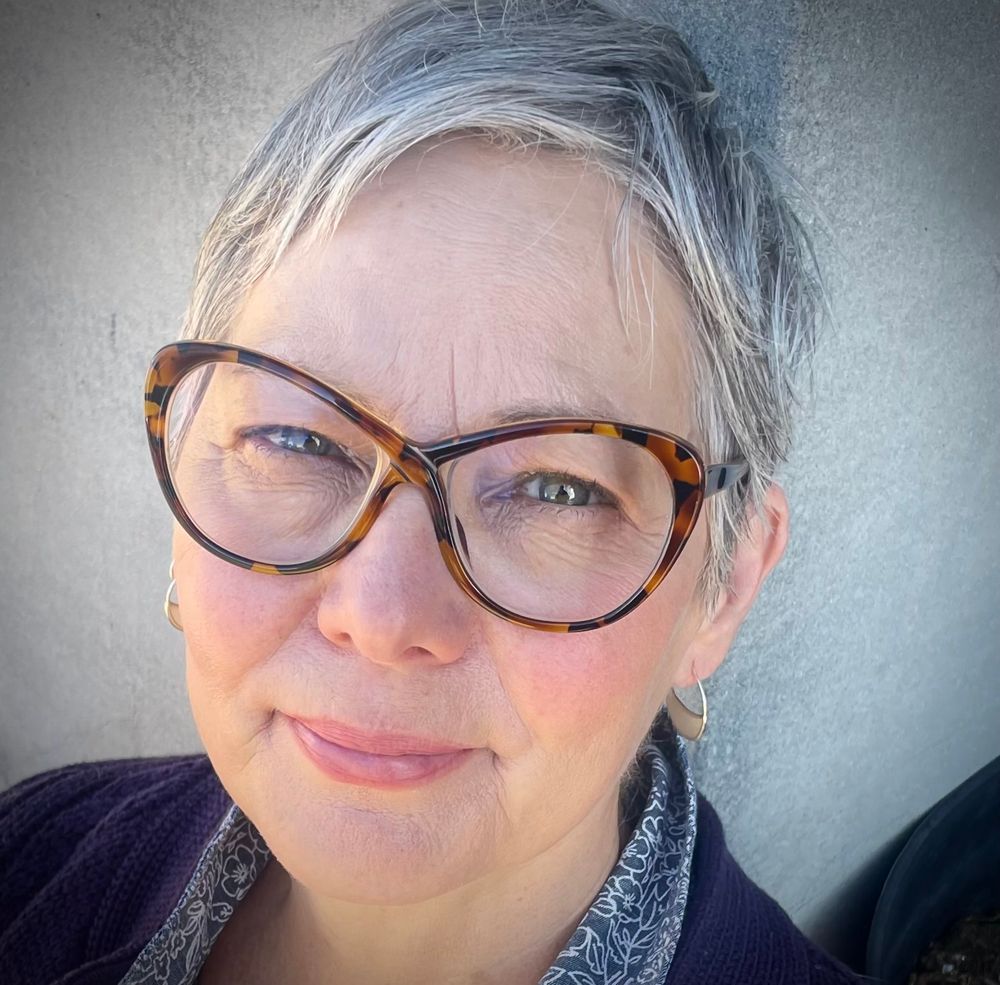 A photo of a SIXTY year old white woman with white hair and glasses. 
