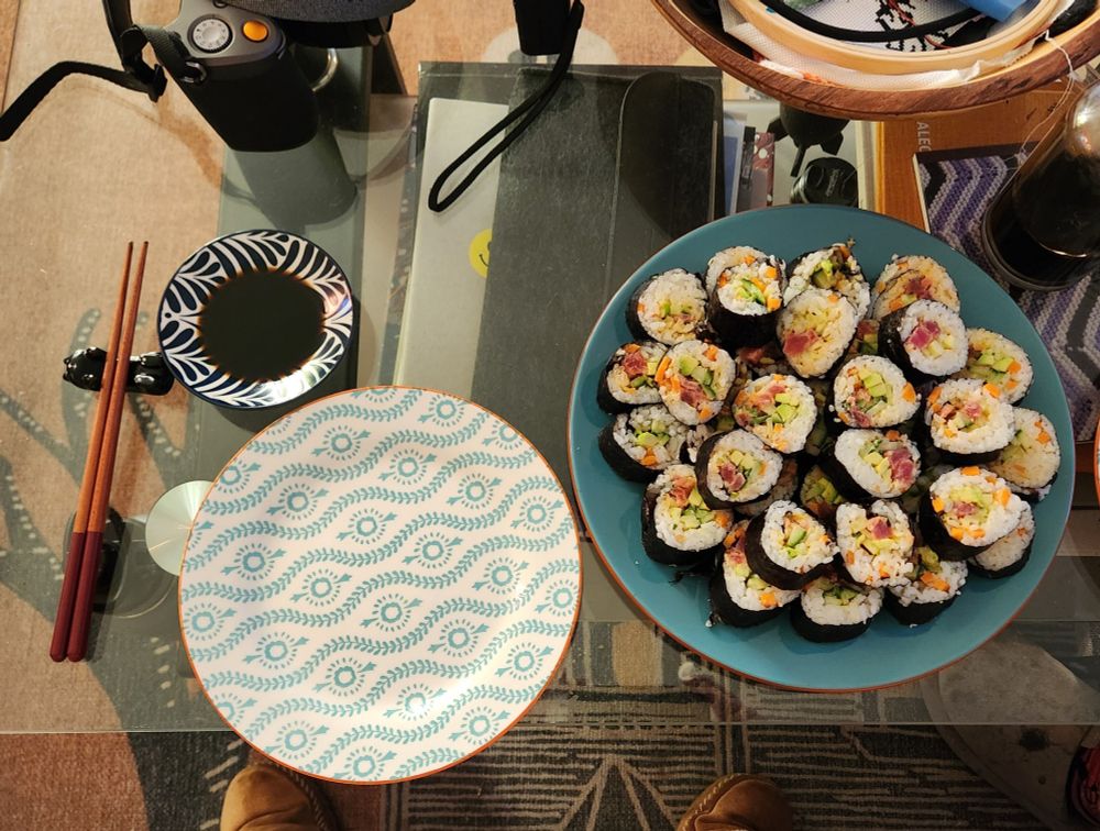 A blue plate full of spicy tuna maki rolls. Next to that plate is a smaller, empty plate and a little dish for soy sauce.