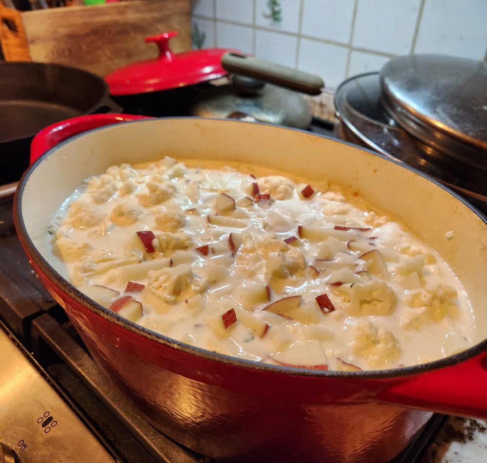 A red Dutch oven on a stove full of chopped potatoes and cauliflower pieces.