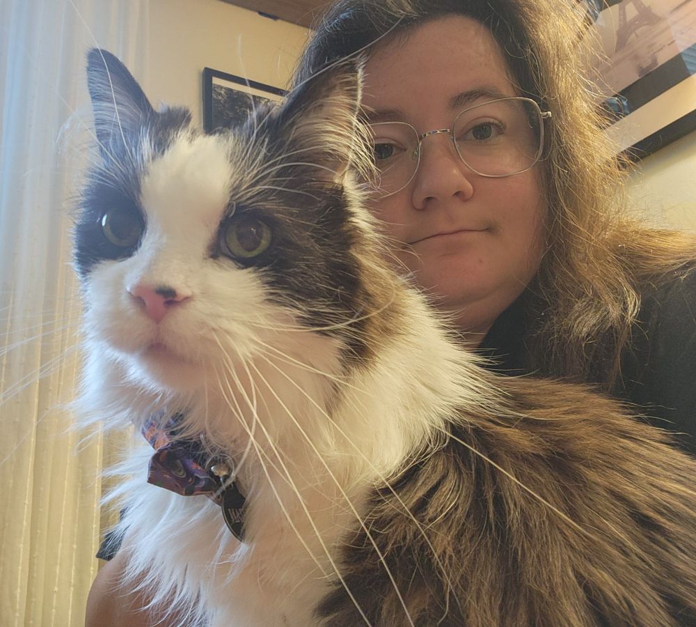 A selfie of a woman and a black and white longhair cat sitting together.