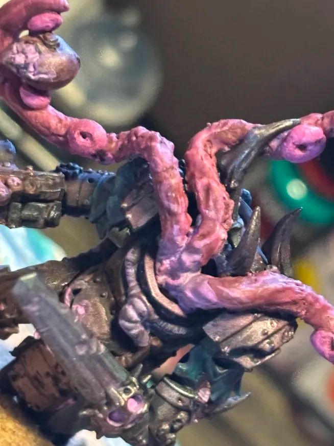 The same model as previous, but zoomed in at the front, showing off the sculpted tentacles, one of which is holding the head of the model. They themselves are holding a gun in one hand and a large sword in the other, they have metallic armour and spikes protruding from it