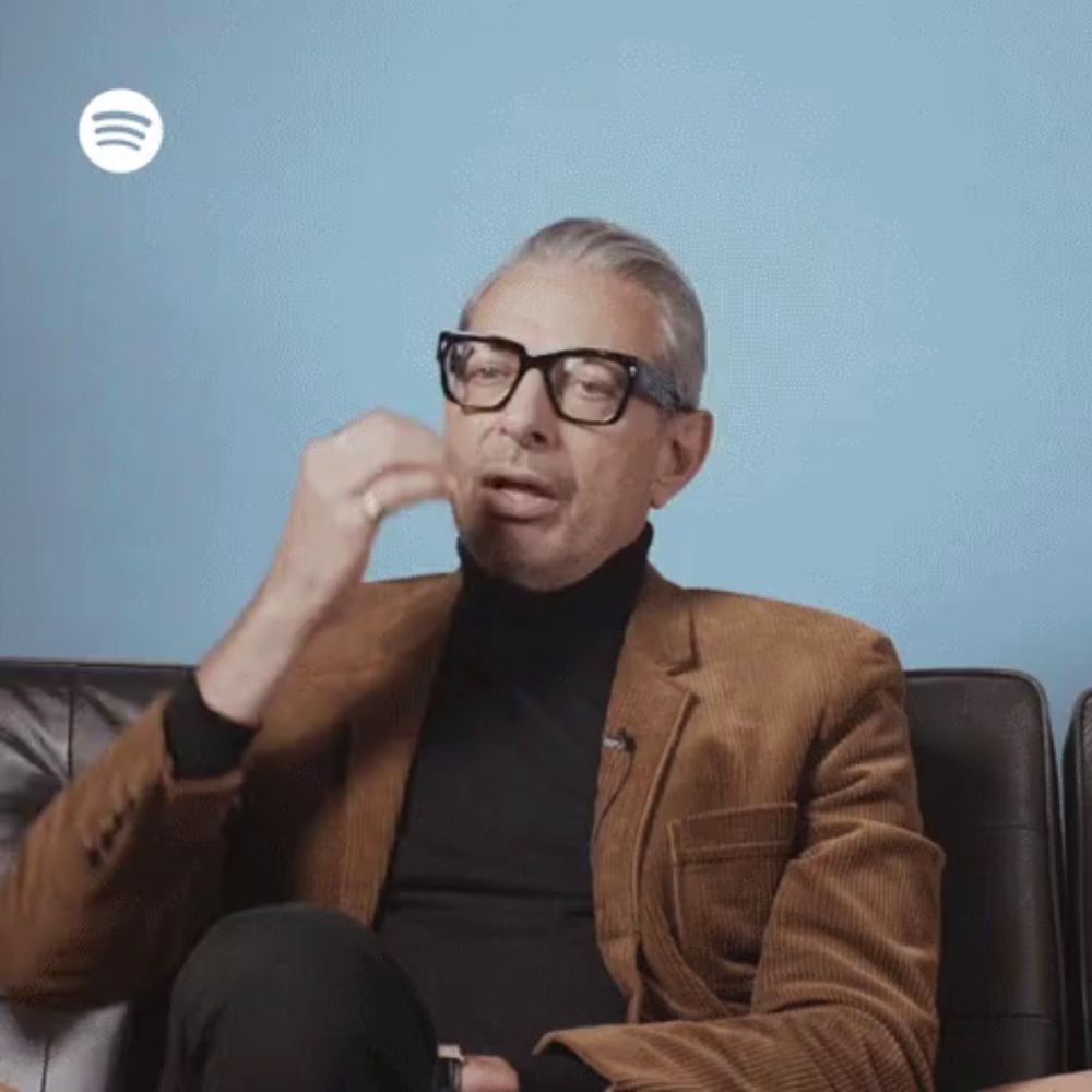 a man wearing glasses is sitting on a couch with a spotify logo in the background