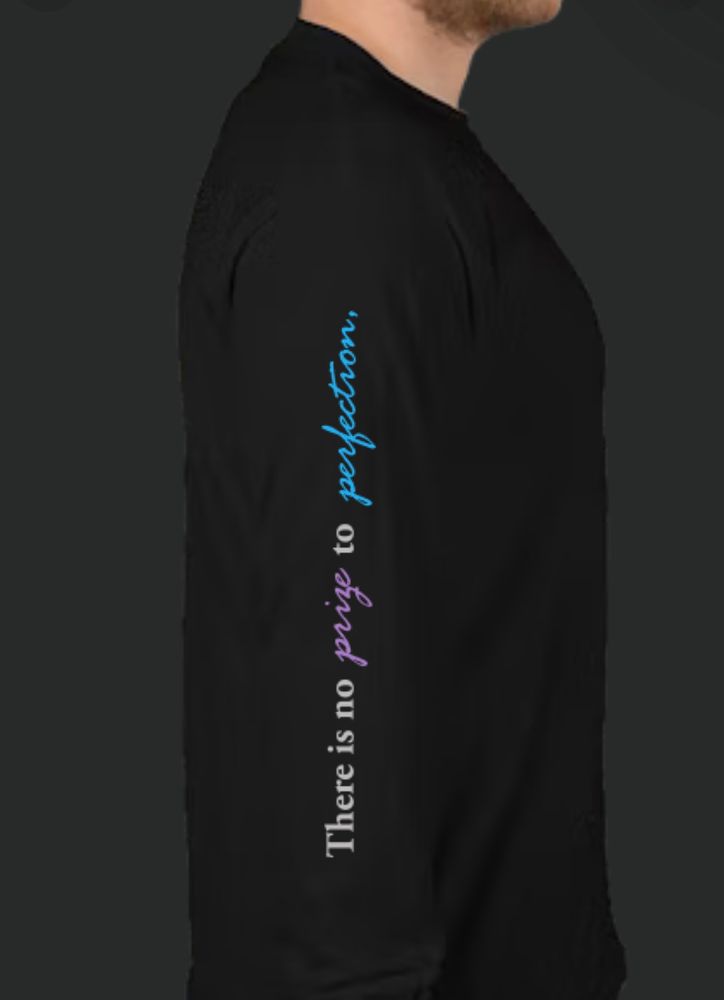 The right sleeve of a long sleeve black shirt that has the words "There is no prize to perfection," up the sleeve. The word prize is lavender and the word perfection is light blue. The rest of the text is light gray.