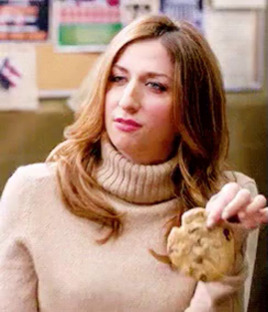 a woman wearing a turtleneck sweater is holding a cookie