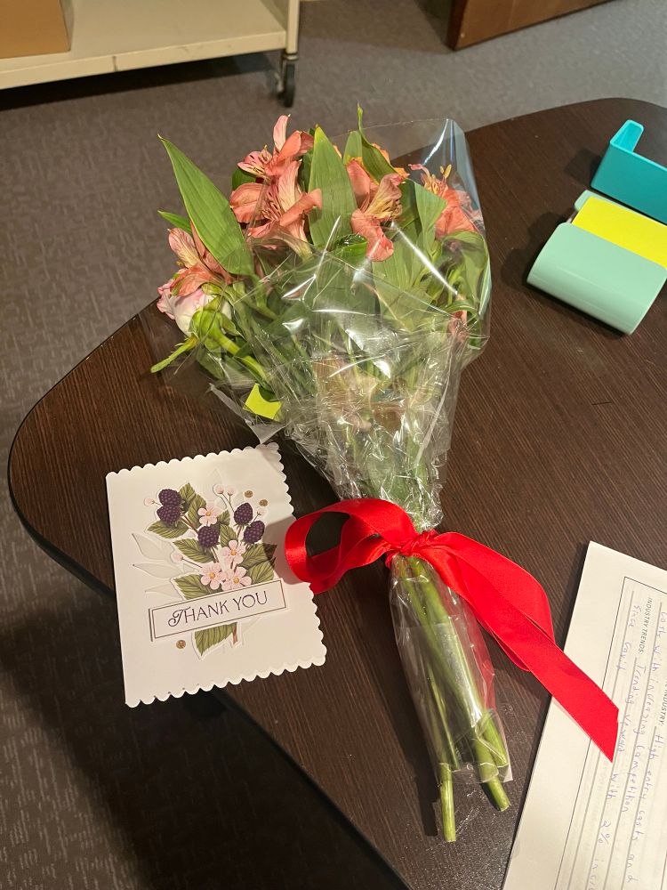 A bouquet of flowers with a Thank You card displayed on a desk.