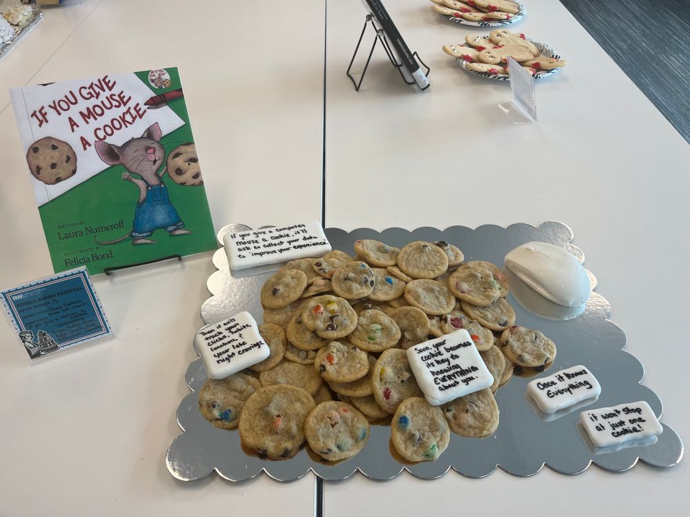 A tray of chocolate chip and M&M cookies on a silver bakery board with a solid white chocolate computer mouse and graham cracker covered in fondant signed scattered throughout that read: If you give a computer mouse a cookie,
it’ll ask to collect your data to “improve your experience.”
Then it’ll track your clicks, your habits, your location, and your late-night cravings.
Soon, your cookie becomes its key to knowing everything about you.
And once it knows everything, it won’t stop at just one cookie.