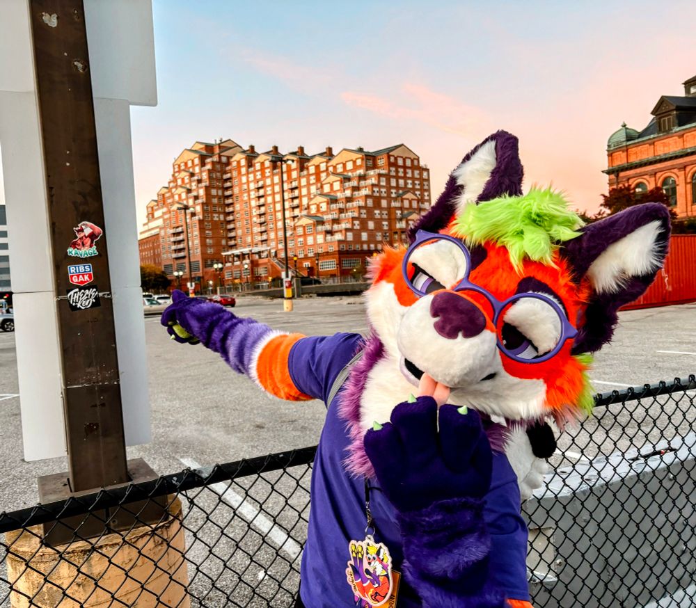 a maned wolf fursuiter in vibrant colors pointing to a parking lot sign post with a ravage (dog) sticker
