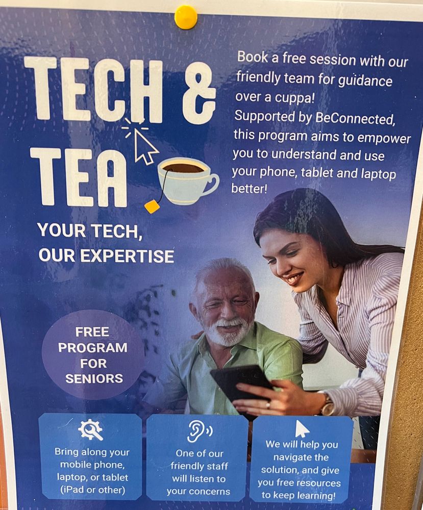 A poster pinned to a cork board at a community center, advertising "Tech and Tea" sessions for seniors. There is a stock photo of a woman leaning over an elderly man and showing him a tablet.