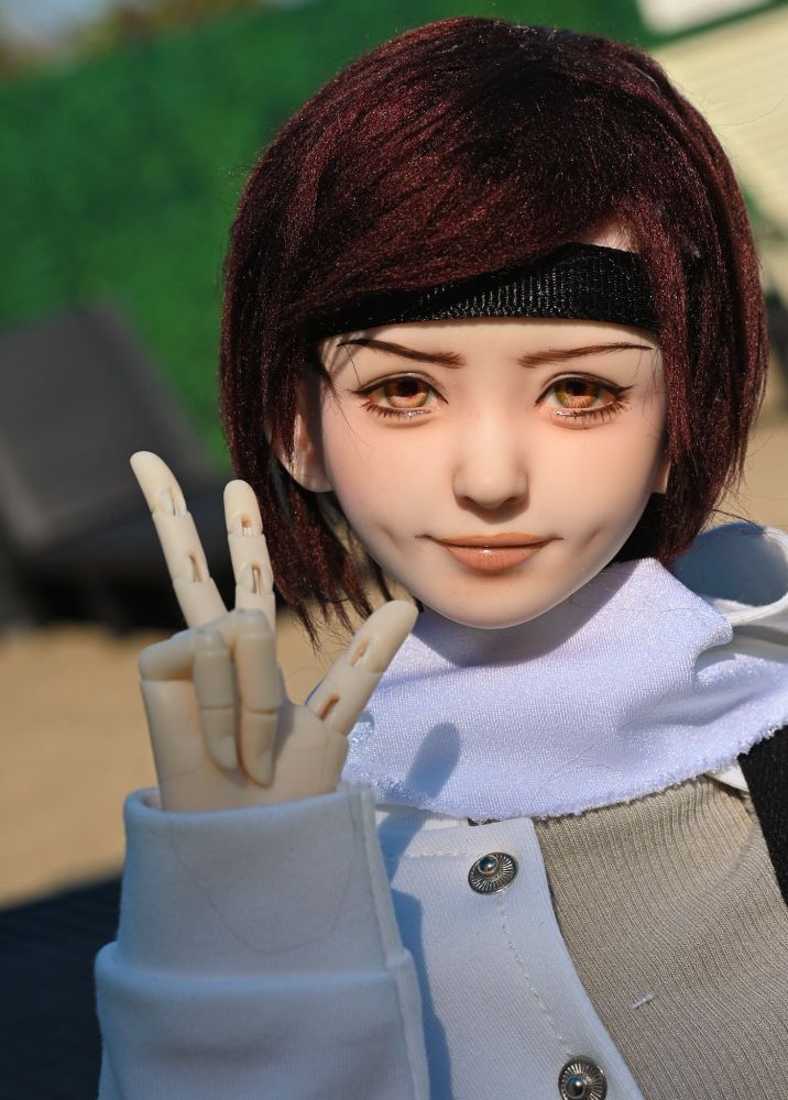 a smirking realistic doll portrait. She has brown hair and is holding up 3 fingers in a modified "peace" sign". The picture is reminiscent of a selfie.