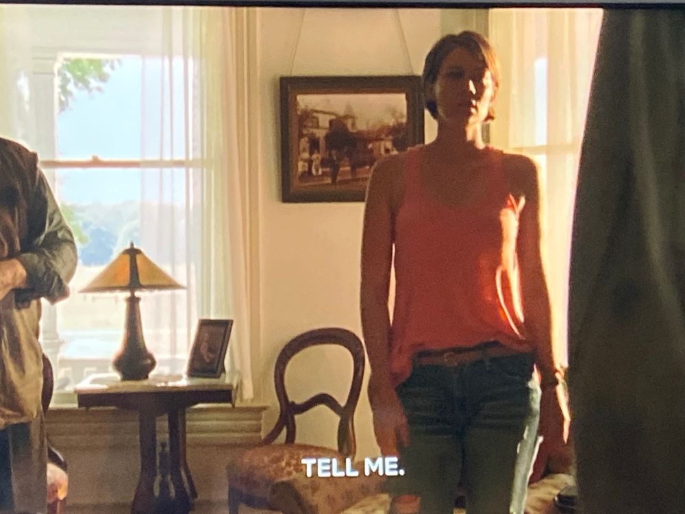 Maggie Greene in a pink/orange half tucked tank top, ripped and bleached skinny jeans, and wearing a flimsy beige belt.
