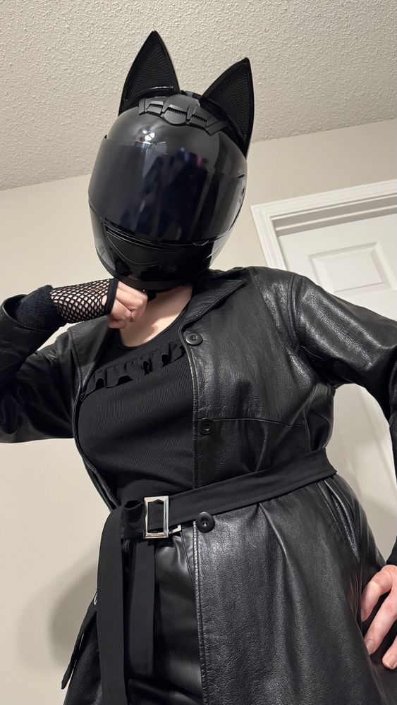 Ocean, wearing her Cat-Eared Biker Helmet, is standing with her left hand on her hip. Her right arm is raised, with hand to chin. She is wearing a black leather jacket and skirt, matching with a black shirt and belts.