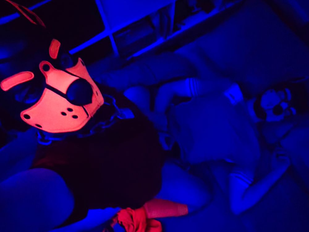 A person (it/its) sat on another person (he/him) lying on a bed; it is riding his cock while he sleeps. They're both wearing football kits and pup hoods.