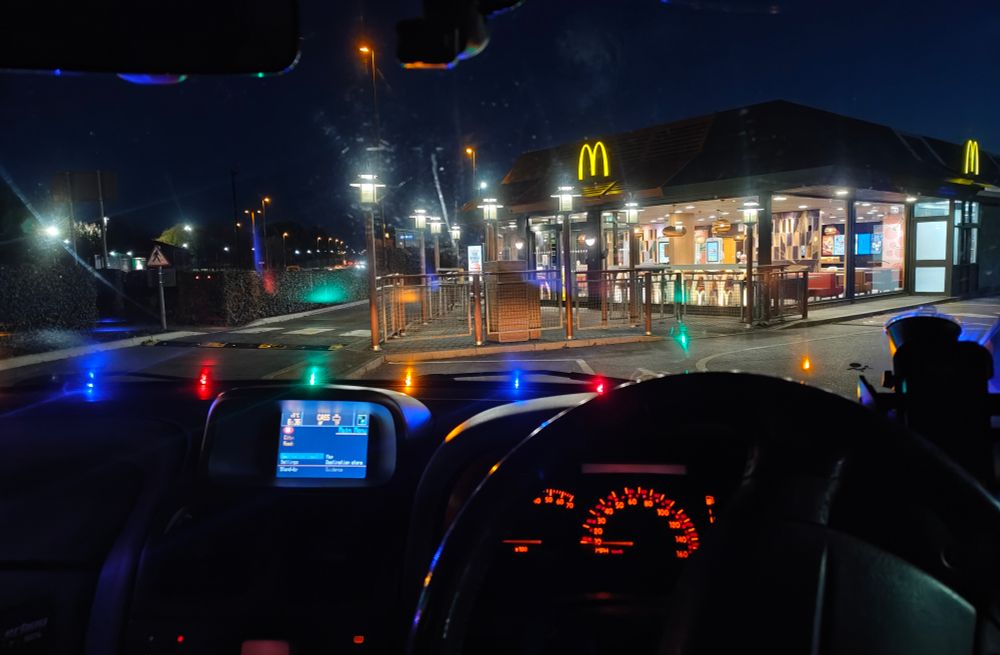 Interior of a car — a 1999 Renault Laguna 2.9 Monaco V6 — looking out towards a McDonald's in the early morning.