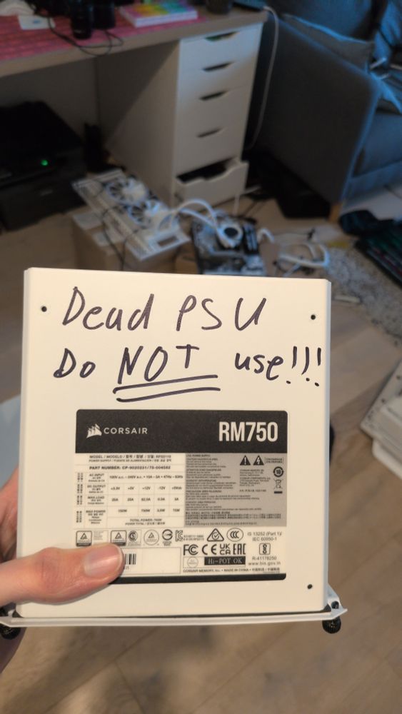 a corsair rm750 power supply, with "Dead PSU Do NOT use!!!" written on it in sharpie. in the background is a partially disassembled PC